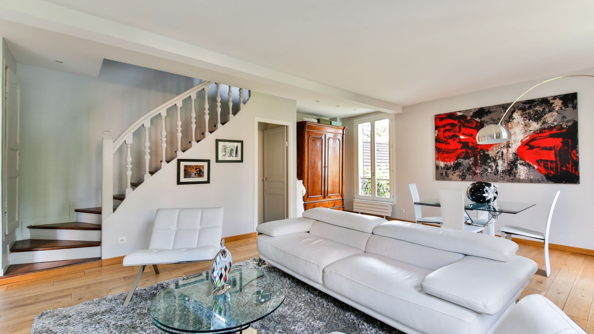 Modern living room with white sofa, curved staircase, and red abstract art