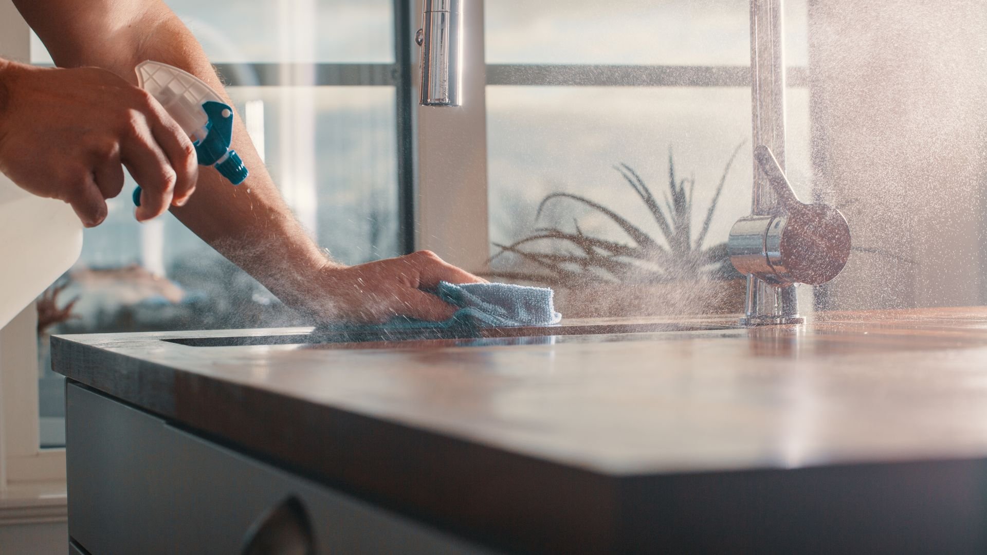 Person cleaning kitchen counter with spray bottle and microfiber cloth